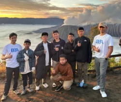 Kelompok peserta berfoto bersama di area pegunungan saat matahari terbit.