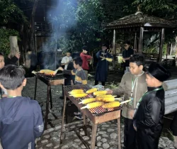 Peserta memanggang jagung bersama di area luar ruangan pada malam hari.