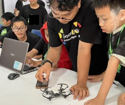 Fasilitator dan peserta mencoba drone kecil di samping laptop.