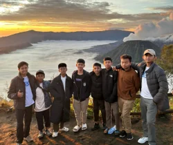 Kelompok peserta berfoto di titik pandang pegunungan saat matahari terbit.
