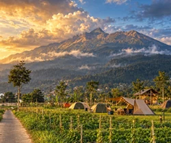 Pemandangan area perkemahan dengan tenda dan gunung saat matahari terbit.